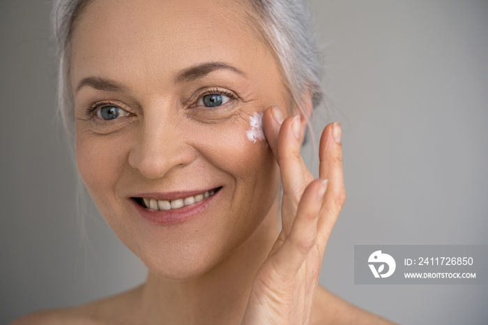 Woman putting cream on facial skin and smiling