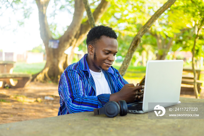 handome african male student browsing online with mobile phone and laptop on school environment