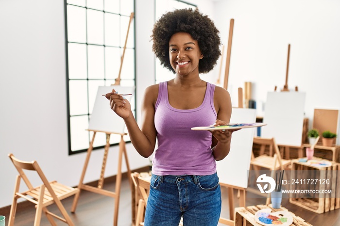 Young african american woman smiling confident holding paintbrush and palette at art studio