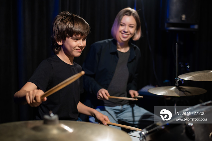 Young caucasian woman teaches a boy to play the drums in the studio on a black background. Music school student