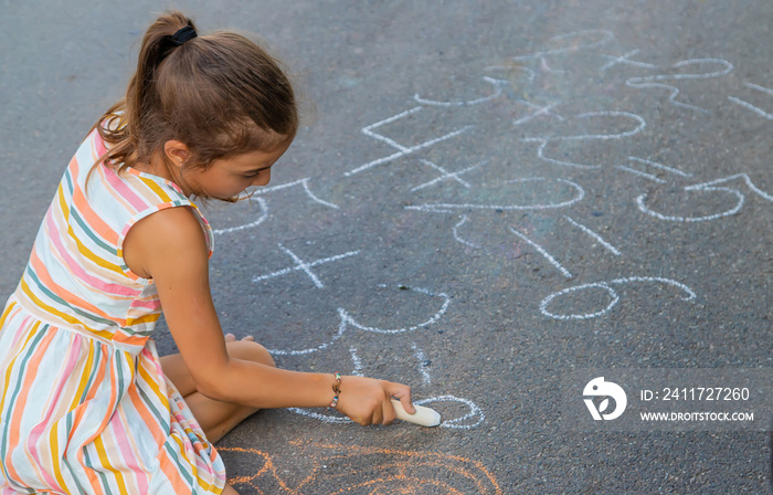 The child is doing chalk lessons on the asphalt. Selective focus.