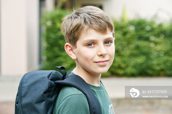 Happy preteen kid boy with backpack or satchel. Schoolkid in on the way to elementary or middle school on warm sunny summer day. Healthy child outdoors on the street in the city .