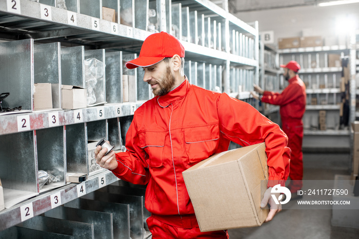 Handsome warehouse worker in red uniform taking some products from the shelves at the storage with car parts