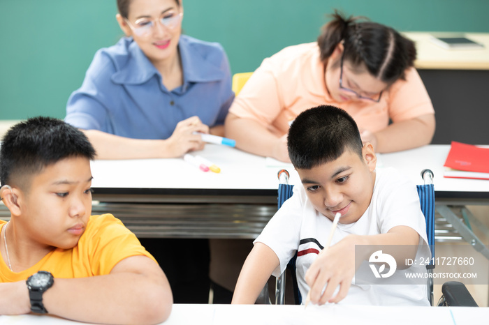 asian disabled kids or autism child learning looking and writing at desks with teacher helping in classroom