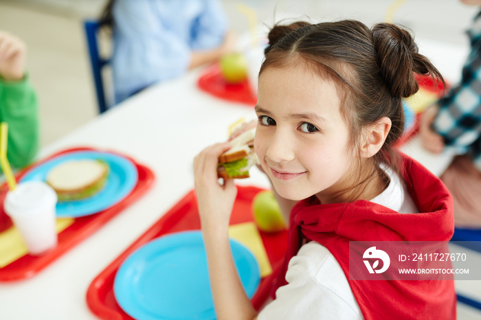 Pretty young schoolgirl eating sandwich at lunch break after classes