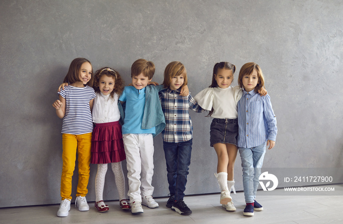 Portrait of happy cute little boys and girls having fun together standing against the backdrop of a gray wall. Children in a variety of bright casual clothes have fun together, hug and pose.