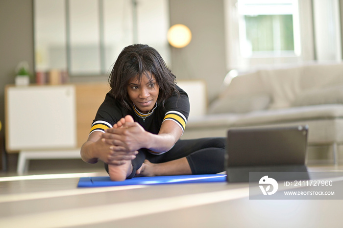 African-american woman doing virtual fitness exercices, digital class on tablet