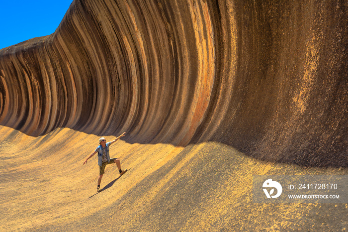 A sporty man enjoying surfing on the Wave Rock, a natural rock formation that is shaped like a tall breaking ocean wave, in Hyden, Western Australia. Happy funny male in Australian outback.