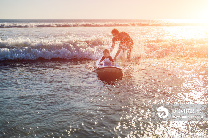 Father teaching his young son how to surf in the sea on vacation or holiday. Travel and sports with children concept