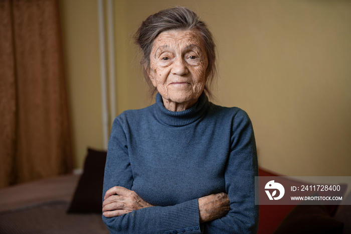 Elderly Caucasian senior grandmother ninety years old looks attentively and smiles, feels happy, large portrait, face with deep wrinkles, gray hair. Theme pensioners, old people and long-lived woman