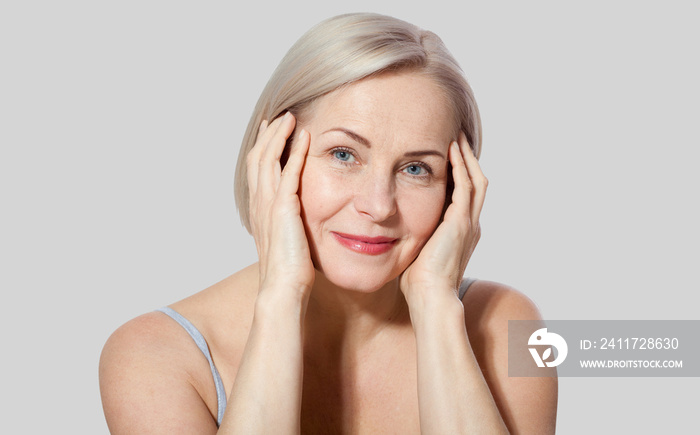 Fifty year old woman is very pleased with her well-groomed face relaxed looking at the camera. Macro face. Realistic images with their own imperfections. Isolated on grey.