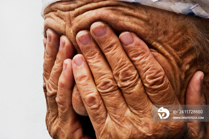 An old saddened grandmother closes her tearful eyes with wrinkled palms close-up. Woman covered her face with hands.