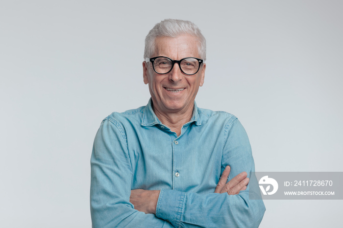 portrait of old man in his 60s in denim shirt crossing arms and laughing