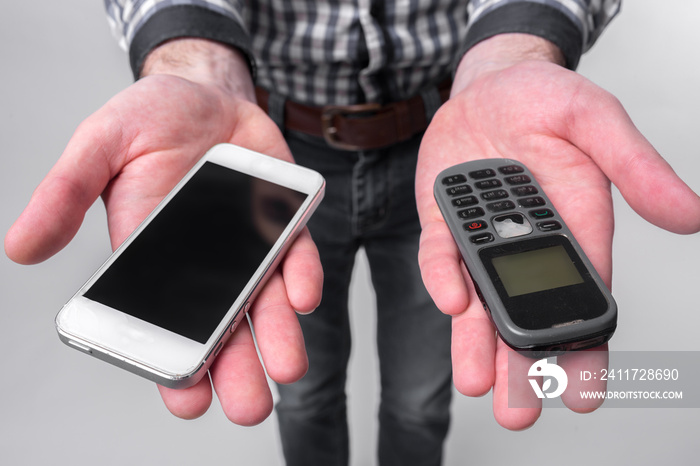 Bearded man isolated on a light background holding a modern smartphone and old cell phone with buttons