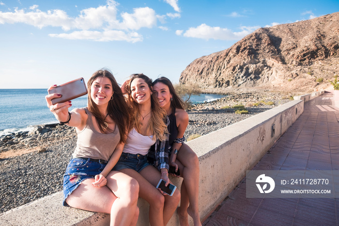 Group of three woman in friendship taking selfies and using phone near the beach on vacation - summer outdoor leisure activity for modern people have fun together with cellular