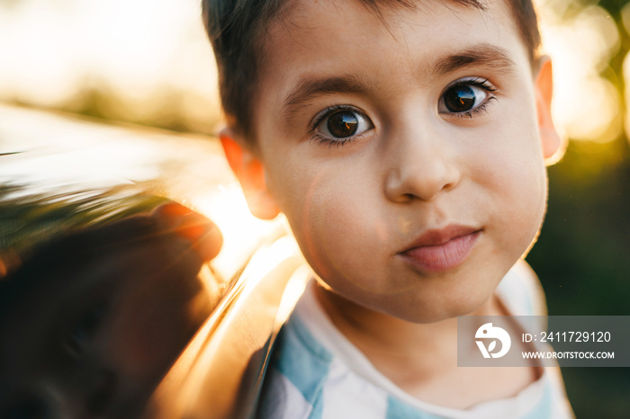 Close up portrait of a little smiling boy sticking his head out the car window and looking at camera. Road trip. Kid life.