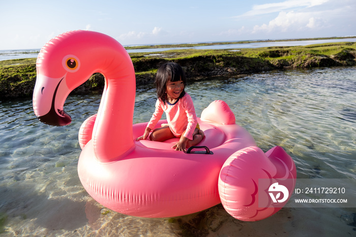 little girl riding a flamingo float on the beach while on vacation to the beach