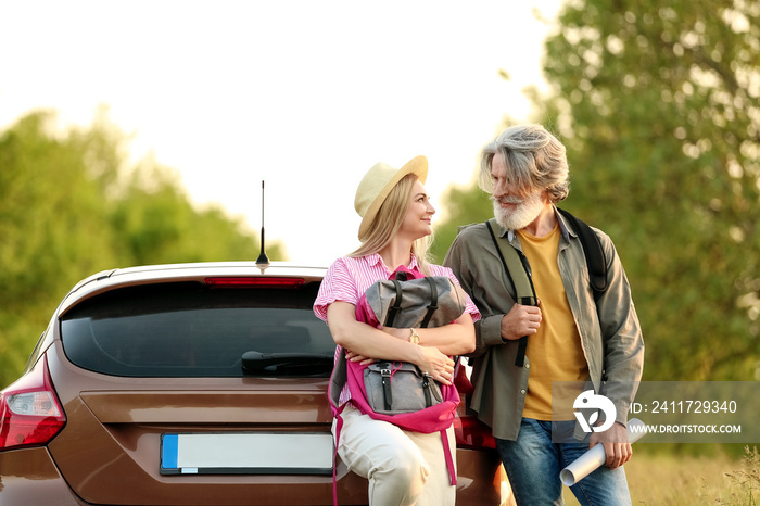 Happy mature couple with backpacks and map near car in countryside