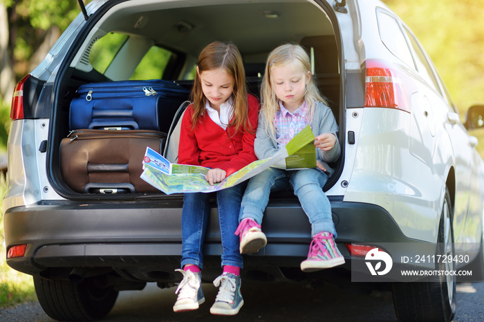 Two adorable little girls ready to go on vacations with their parents. Kids sitting in a car examining a map.