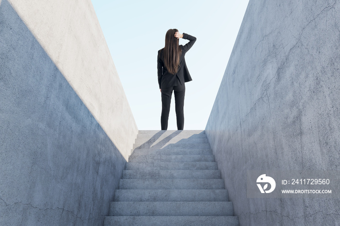 Back view of thoughtful businesswoman standing on top of abstract concrete stairs to success with sunlight. Growth and leadership concept.