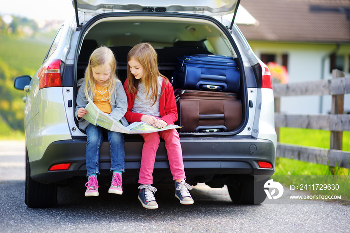 Two adorable little sisters exploring a map before going on vacations with their parents