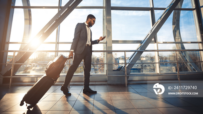 Black Businessman Using Mobile Phone Walking In Airport, Panorama, Side-View