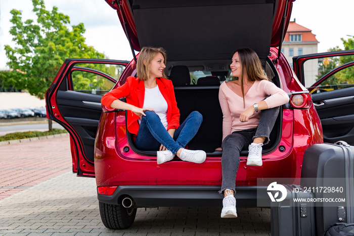 Two girls chat while sitting in open trunk of car