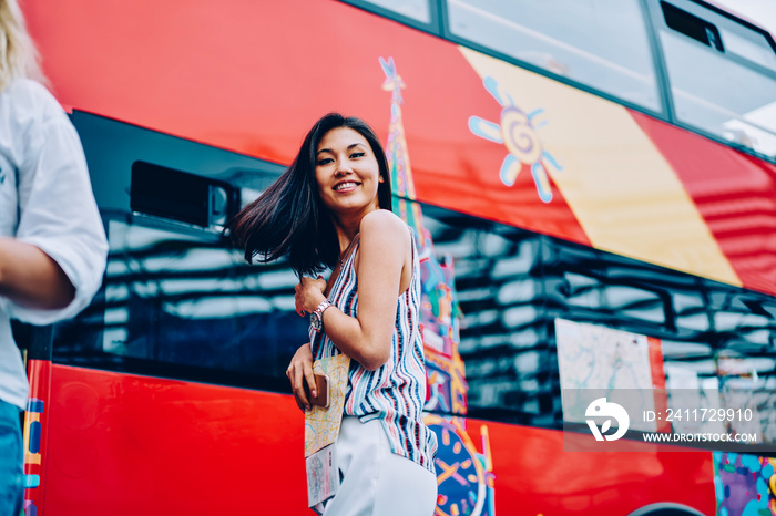 Portrait of smiling asian girl holding map waiting for excursion to Moscow landmarks, happy female tourist standing near sightseeing bus planning to explore city on transport looking at camera