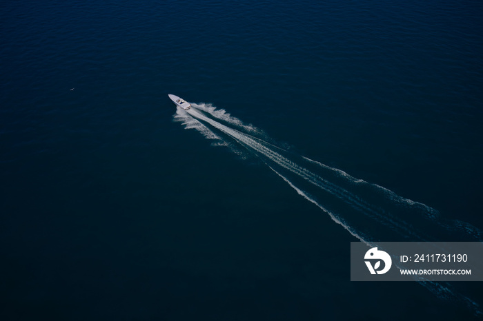 White speedboat fast moving diagonally on dark blue water aerial view.