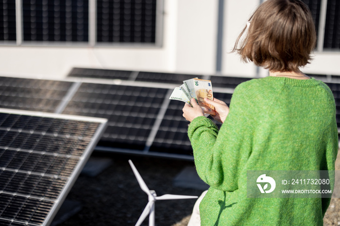 Woman counts euro banknotes saved due to the generation of energy from a solar power plant installed on her house rooftop. Concept of investment in alternative energy