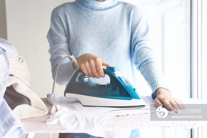 Young woman ironing clothes at home