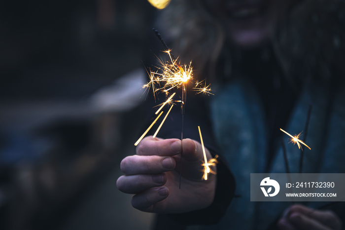 Burning sparklers in the hands of a young woman in the dark.