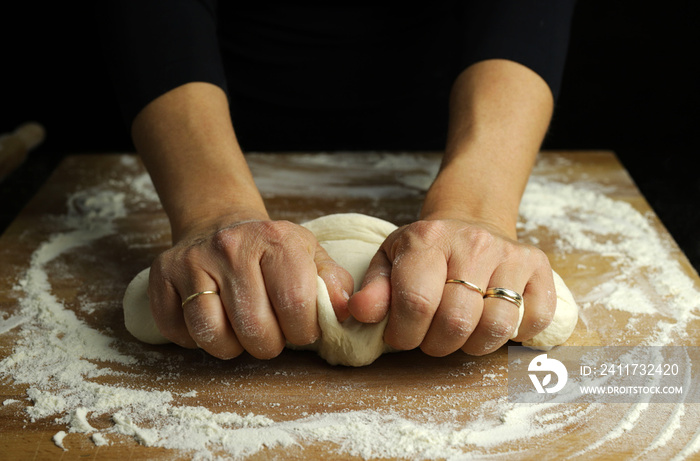 Preparare la tradizionale pasta fatta in casa. Primo piano delle mani della donna che impastano pasta fresca per produrre pane o pizza su una tavola infarinata