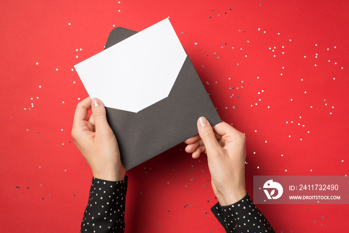 First person view overhead photo of woman hands holding black envelope with white card inside isolated on the red background with confetti