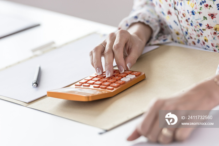 Businesswoman using orange calculator in the office as she sits at her desk, close up view of her hands.