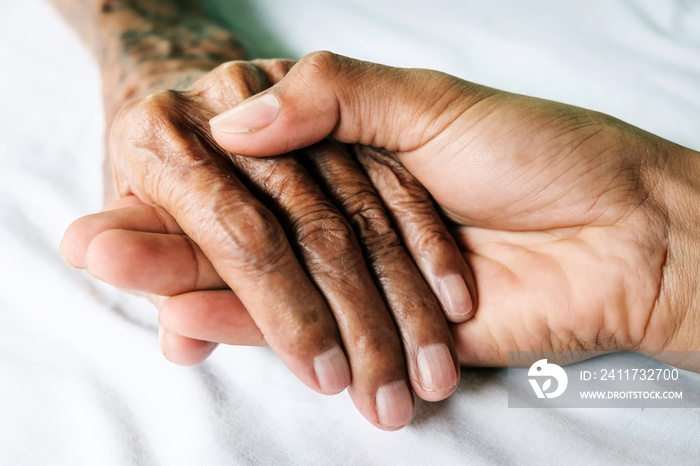 Hands of an old man with wrinkled and wrinkles on a white bed in a hospital.