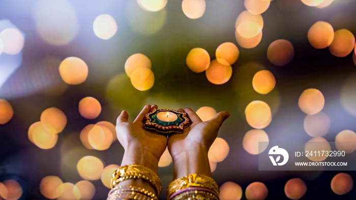 Happy Diwali - Woman hands with henna holding lit candle isolated on dark background. Clay Diya lamps lit during Dipavali, Hindu festival of lights celebration.