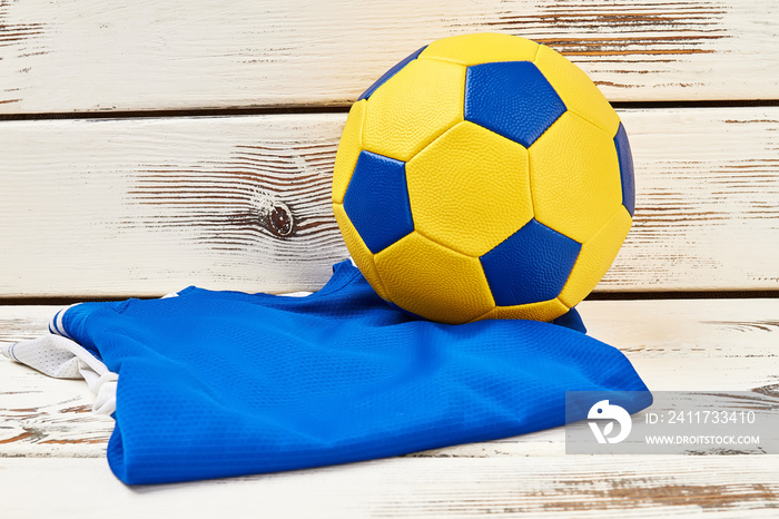 Soccer ball and folded uniform on wooden background. Blue and yellow. Attributes of popular game.
