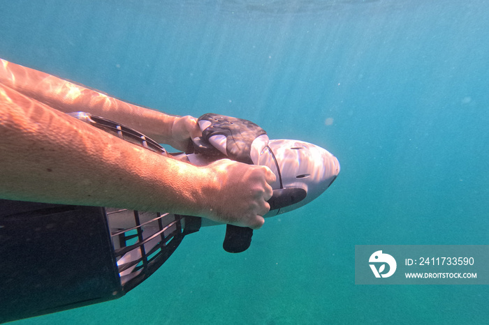 Underwater photo of arms of sea diver operating a battery driven motorised sea scooter in deep blue crystal clear sea