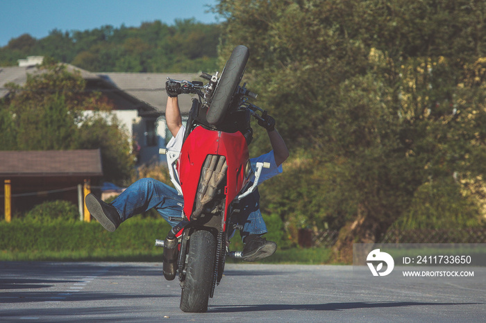 Motorcycle stunt man practicing on a home parking lot on a red and white motorcycle. Frontal view of a stuntman making a wheelie on a motorcycle.