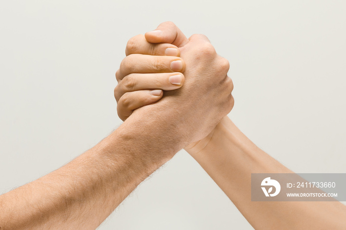 Friends greetings sign or disagreement. Two male hands competion in arm wrestling isolated on grey studio background. Concept of standoff, support, friendship, business, community, strained relations.