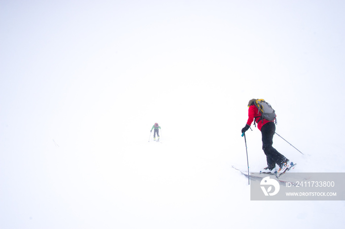 Two skiers struggling into a snow storm during a whiteout in the mountains