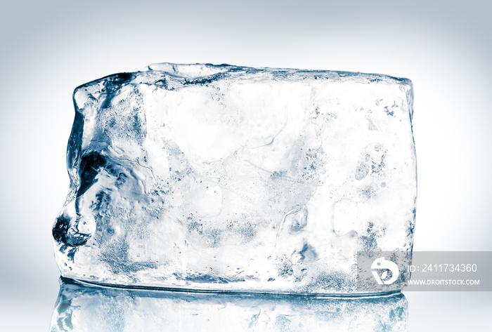 Crystal clear natural ice block in cold blue tones on reflective surface. Clipping path included.