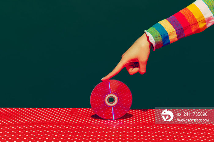 Female hand holding cd disk isolated on green and red background. Vintage, retro fashion style. Pop art photography