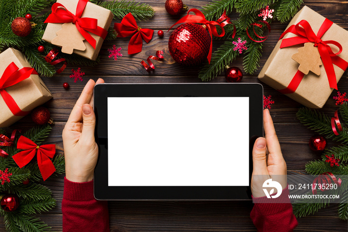 Christmas online shopping from home, female hands holding tablet pc with blank white display top view. woman hand holding tablet with blank screen, Christmas tree and gifts on background