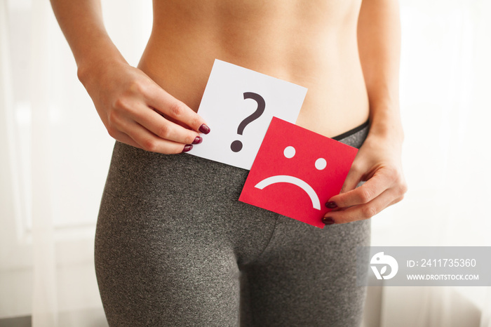 Vaginal or urinary infection and problems concept. Young woman holds paper with sad smile above crotch