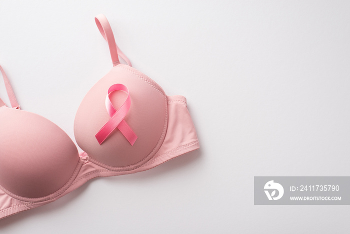 Top view photo of pink ribbon symbol of breast cancer awareness attached to pink bra on isolated white background with copyspace