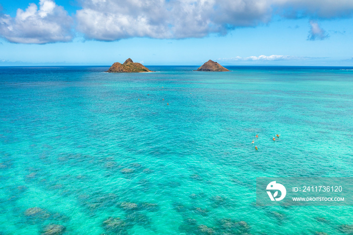 Aerial drone view of the Mokolua islands off the coast of Lanikai Beach in Oahu, Hawaii, USA. Water is turquoise, reef is visible, few white clouds in sky.