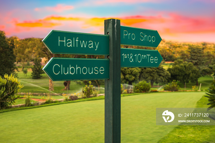 Golf course direction signs on fairway and colourful sunset in the background