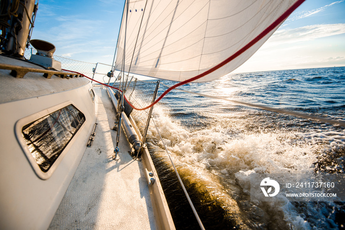 White yacht sailing at sunset. A view from the deck to the bow and sails. Waves and clouds. Baltic sea